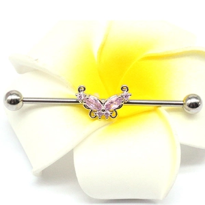 Detail view of butterfly industrial barbell earring with pink zircon on a plumeria flower