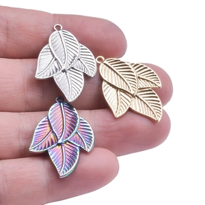Leaf-shaped stainless steel pendants in silver, gold, and rainbow finishes shown held