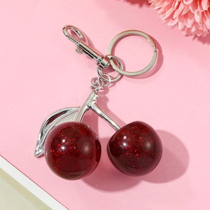 Close-up of glittery dark red cherry keychain with silver metal leaves on pink backdrop