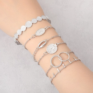 Detail of silver layered bracelet set featuring butterfly and coin charms on a model wrist