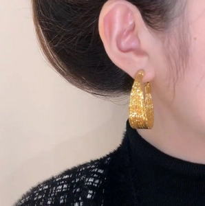 Detail of gold U-shaped hoop earrings with woven texture worn by a fashion model