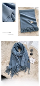 Detail of light blue scarf with fringe tassels and woven brand label on soft plush rug