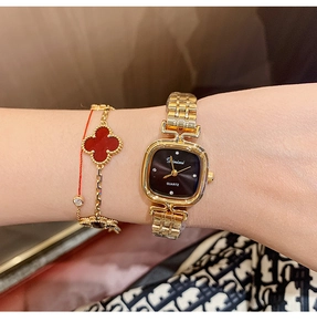 Close-up of golden square quartz watch with matching red clover leaf charm bracelet