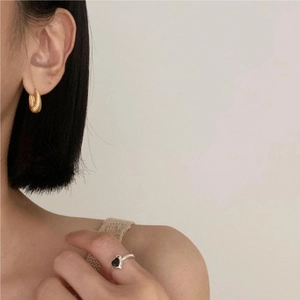 Detail of twisted gold hoop earrings and a silver ring with a black heart on a model