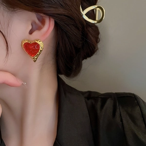 Macro detail of vintage heart earring with red finish and hammered gold metal frame