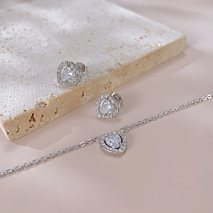 Detail of silver heart-shaped pendant and earrings with zircon halo on stone texture