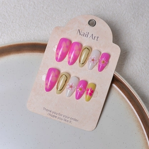 Detail of almond-shaped press-on nails with 3D white floral art and gold foil accents