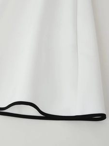 Detailed close-up of white dress hem featuring contrasting black piping and smooth fabric