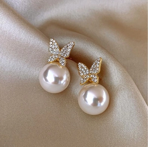 Detail of gold butterfly earrings with sparkling crystals and large white pearls