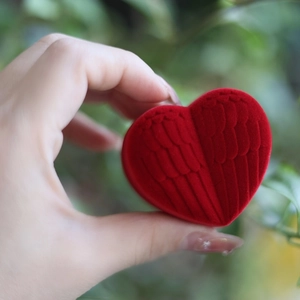 Detail of a red heart-shaped jewelry box with wing texture held in a hand