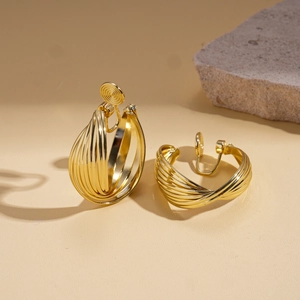 Detail of twisted gold metal clip-on earrings with soft round ear pads on stone