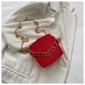 Detail of red hard shell clutch bag with chunky chain and gold metal strap on white blazer