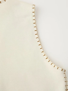 Detail of brown contrast stitching on the neckline of a cream knit vest top