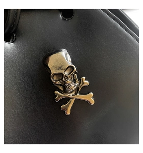 Detailed macro view of a vintage metal skull and crossbones stud on black leather bag