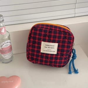 Close-up of quilted red and blue checkered cosmetic bag with yellow zipper on window sill