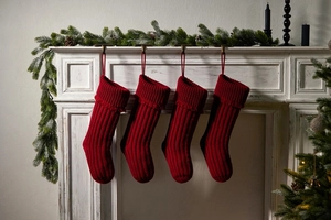 Close-up of four red knitted Christmas stockings hanging on a white vintage fireplace