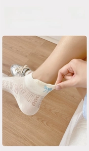 Detail of white mesh socks featuring blue bow embroidery and elastic ribbed cuffs