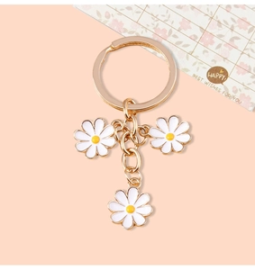 Detailed macro view of gold-tone keychain with three delicate white daisy floral charms