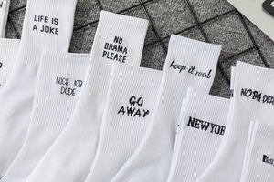 Detail of white mid-calf sports socks featuring various black letter slogans and ribbed cuffs