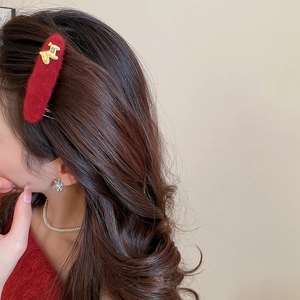 Detailed view of a red velvet hair clip with a gold puppy pendant on a female model