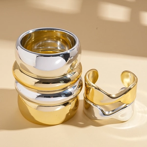 Stack of gold and silver thick round rings and wavy twisted bangles on beige background