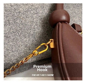 Close-up of vintage gold metal hook and chain detail on dark brown leather handbag