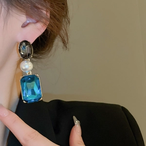 Detail of vintage earring featuring oval dark gem, white pearl, and blue square stone
