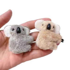Plush koala hair clips in grey and beige colors shown on a palm for size reference