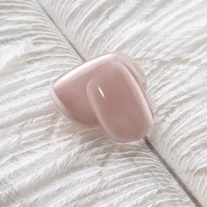 Glossy nude pink short press-on nails displayed on soft white feathers background