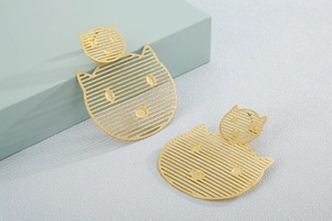 Detail of golden hollowed cat-shaped earrings with striped texture on blue pedestal