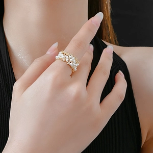 Dettaglio anello intrecciato con perle e sfere dorate indossato all'indice su maglia nera