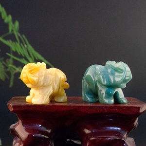 Polished natural jade elephant statues in yellow and green on a dark wood base