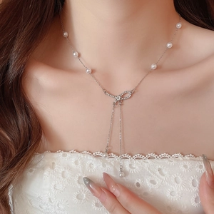 Detail of silver pearl necklace featuring a sparkling diamond-encrusted bow pendant