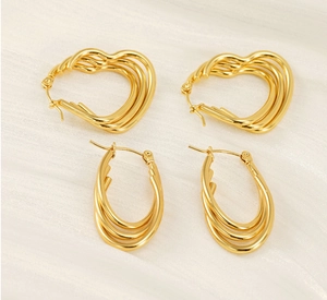 Detailed macro shot of 18k gold multilayer heart and oval hoop earrings on white silk