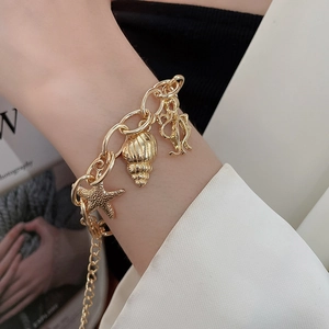 Close-up of a gold chunky chain bracelet with starfish and seashell charms on a wrist