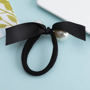 Black elastic hair tie with handmade fabric bow and two large white pearls on blue background