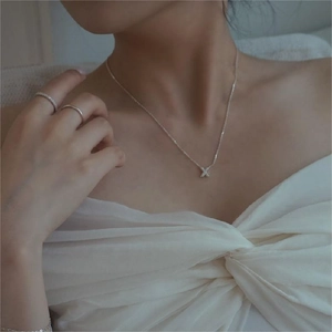 Close-up of minimalist S925 sterling silver X-shaped pendant necklace and ring on model
