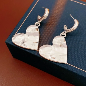 Macro shot of silver heart pendant C-shaped earrings with textured hammered finish