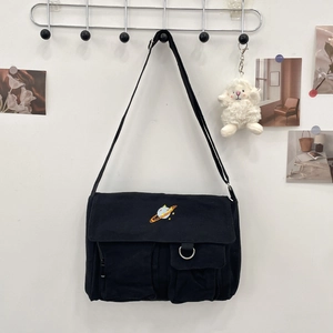 Detail of black canvas messenger bag featuring planet embroidery and metal D-ring pocket
