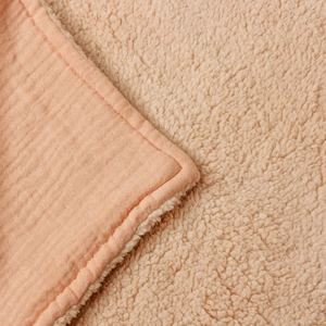 Detail of pink muslin cotton blanket with warm cream faux lambswool lining