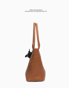 Detail of brown woven leather tote bag with intricate texture and black cat charm decoration
