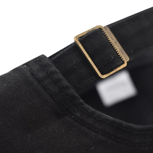 Detailed macro view of the adjustable bronze metal buckle on a black washed cotton cap