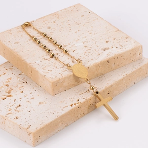 Gold stainless steel beaded cross necklace displayed on beige travertine stone blocks
