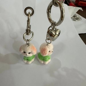 Detail of two mini flocked white dog keychains wearing green outfits and heart charms