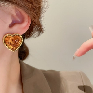 Close-up of amber heart-shaped resin earrings with irregular gold-tone metal edges
