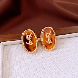 Macro detail of oval gold-tone earrings with amber resin and vintage metal logo