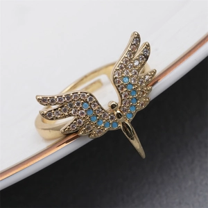 Golden angel wing open ring with blue and white zircon stones on a gray surface