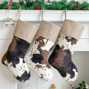Three plush cow print Christmas stockings hanging on a white mantle with greenery