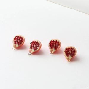 Detailed view of DIY resin pomegranate fruit pendants with red seeds and golden rings