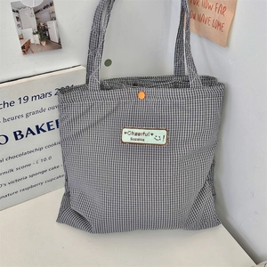 Detail of checkered tote bag featuring a mint green patch and orange snap closure button